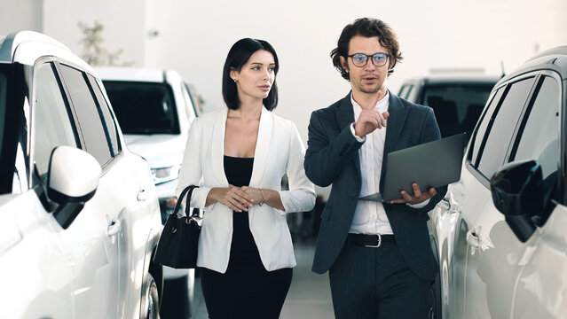 Professional car dealer presenting vehicle options to potential buyer in modern showroom, showcasing sleek cars and engaging atmosphere