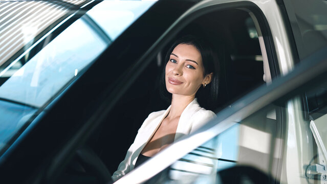 Woman in stylish attire is sitting inside a car at a showroom, showcasing the vehicle's interior and modern design features with natural light