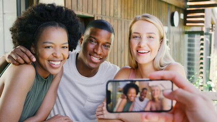 Multi-Cultural Friends Posing For Selfie On Mobile Phone Outdoors At Home