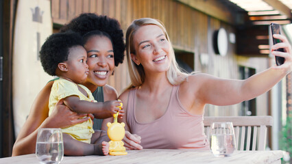 Same Sex Family With Two Mums Playing With Young Daughter Outdoors At Home