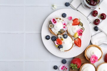 Delicious dessert. Tartlets with cream, berries and flowers on white tiled table, flat lay. Space for text