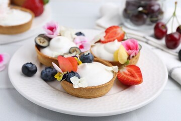 Delicious dessert. Tartlets with cream, berries and flowers on white tiled table, closeup