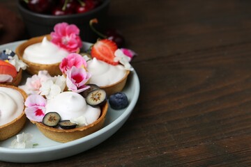 Delicious dessert. Tartlets with cream, berries and flowers on wooden table, closeup. Space for text