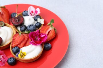 Sweet tartlets with berries and flowers on grey table, closeup. Delicious dessert
