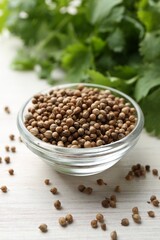 Coriander seeds in bowl and fresh cilantro leaves on light wooden table, closeup
