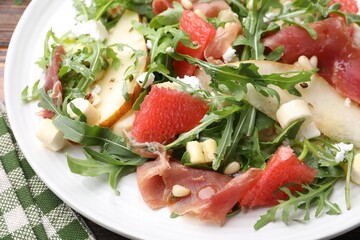 Tasty salad with arugula, prosciutto, cheese, pear, grapefruit and nuts on table, closeup