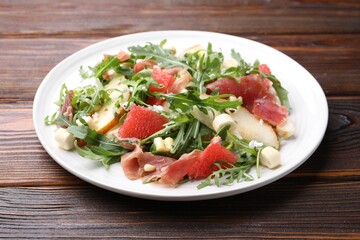Tasty salad with arugula, prosciutto, cheese, pear, grapefruit and nuts on wooden table, closeup