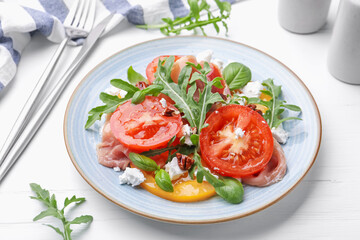 Tasty salad with arugula, cheese, tomatoes, nuts and prosciutto on white wooden table, closeup