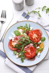 Tasty salad with arugula, cheese, tomatoes, nuts and prosciutto on white wooden table, flat lay