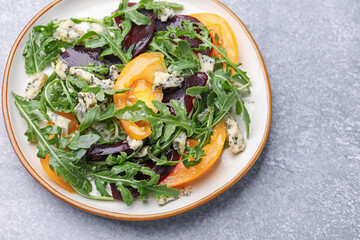 Tasty salad with arugula, blue cheese and vegetables on grey textured table, above view