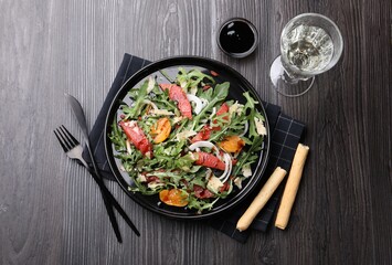 Tasty salad with arugula, cheese, grapefruit, vegetable and balsamic sauce served on dark wooden table, flat lay