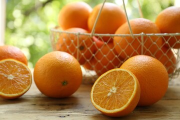 Fresh whole and cut oranges on wooden table against blurred green background, closeup