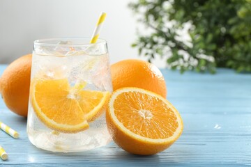 Sparkling water with orange slices in glass and fresh fruits on light blue wooden table, closeup. Space for text