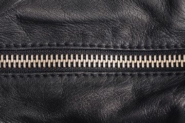 Closeup of metal zipper on black leather surface. Fashion detail of jacket or bag. Texture of wrinkled leather with shiny teeth. Stylish garment material. Seam and fabric structure under studio light.