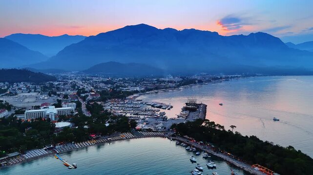 Beautiful resort city of turkey at sunset time. Drone flight over the beaches and yacht club. Mountain silhouettes at backdrop. Kemer, Turkey.