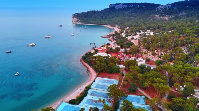 Footage over the coast of the Mediterranean Sea with houses and multiple trees. Some boats are on the waterscape near the shore. Kemer, Turkey.