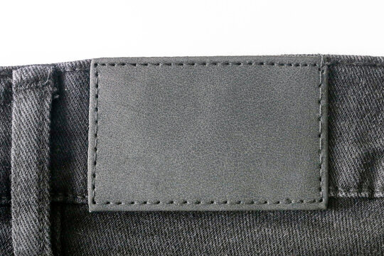 Jeans label closeup on black denim. Blank leather patch on waistband. High resolution texture for branding or design. Fashion apparel detail. Sewing stitches and textile fabric.