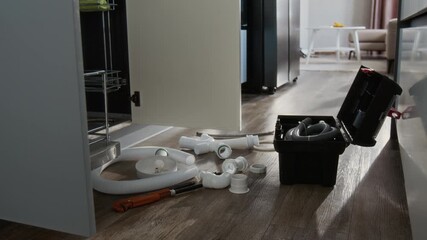 Side view closeup shot of repairing and maintenance concept with pvc pipes and open toolbox on floor by kitchen cabinet, copy space