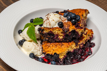 White plate with piece of fresh baked blueberry cobbler and ice cream on wooden background, closeup. Homemade berry cobbler ready to eat