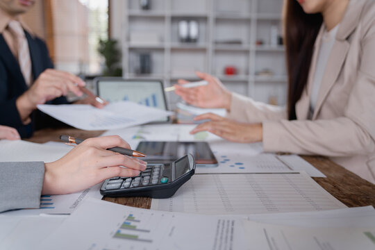 Business colleagues are working together, analyzing financial figures using a calculator, printed reports, and digital tablets, collaborating on a project in a modern office