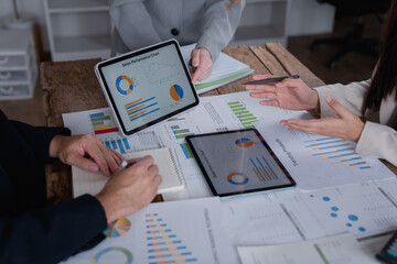 Business colleagues are collaborating on a project, analyzing financial data displayed on digital tablets and paper charts, discussing strategies and performance during a productive meeting