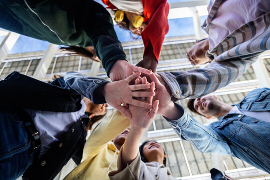 Low angle view of young people stacking hands outdoor. Student friends showing support. Youth community concept.