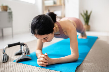 Young fitness woman doing push ups while exercising on a yoga mat at home. Sports and healthy lifestyle concept.