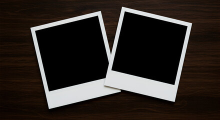 Two blank instant photo frames lay on a dark wooden surface, perfect for your design projects and mockups, showcasing a clean and minimalist aesthetic.