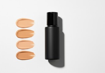 Obraz premium Black bottle of foundation with swatches of different skin tones on white background