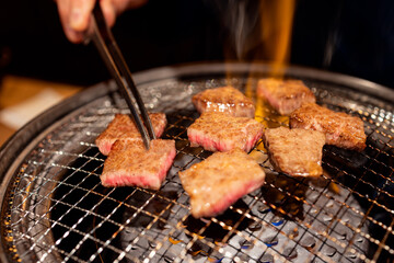 Grilling premium A5 Wagyu beef slices on traditional metal grate over open flame with juicy marbling texture and appetizing surface in Japanese yakiniku style