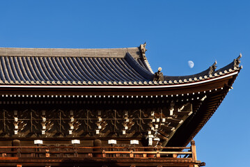 Obraz premium Roofline of Chion-in Temple Sanmon Gate in Kyoto with traditional Japanese ornamentation captured in warm light beneath a blue sky with visible half moon
