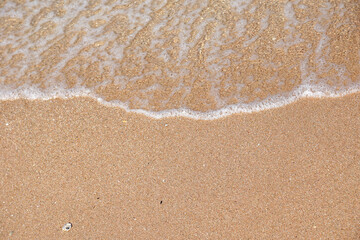Minimal top view of gentle ocean wave washing onto smooth sandy beach with ample copy space. Tranquil natural seascape background.