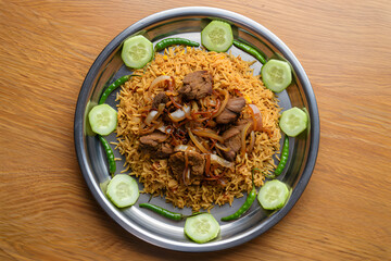Overhead shot of delicious lamb mandi food, garnished with cucumbers and chilies, served on a metallic platter.