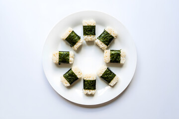 Overhead shot of eight rice and seaweed snacks arranged on a white plate; minimalist food photography.