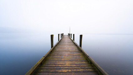 Fototapeta premium Wooden Pier Extending into a Misty Calm Lake with Wooden Posts dock jetty