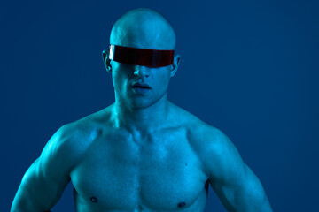 Intense man in futuristic sunglasses showcasing a strong physique against a cool blue backdrop. A captivating expression evokes a sense of mystery and intrigue.
