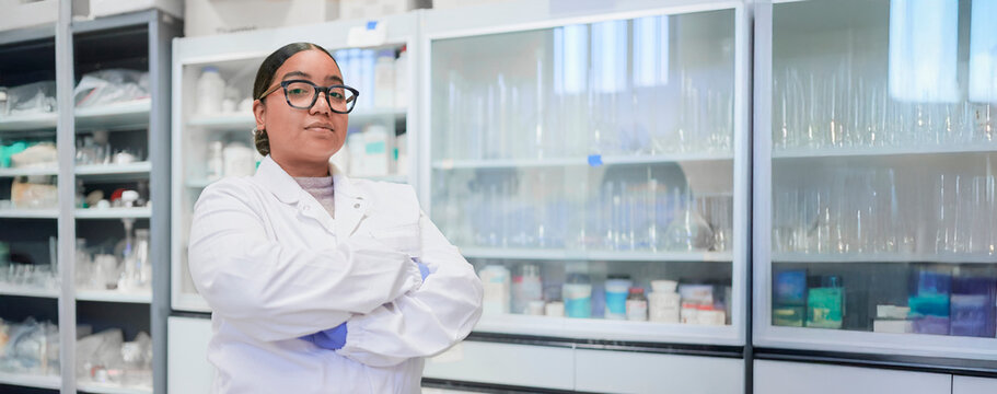 Confident Dominican woman scientist stands proudly in a professional laboratory environment, wearing a clean white lab coat, in front of shelves and cabinets and research equipment.