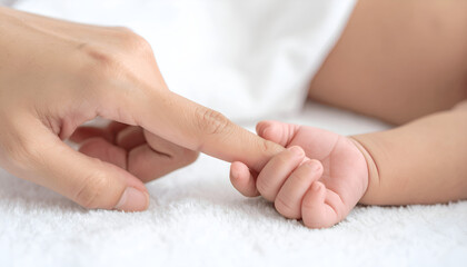 Fototapeta premium Gentle bond of love: Adult hand holding baby's tiny finger on soft white surface