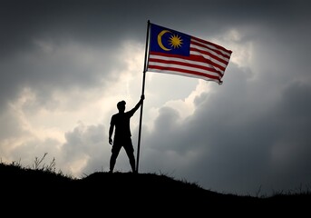 Silhouette of Man Holding Malaysian Flag on Hilltop – Patriotic Scene Against Dramatic Sky