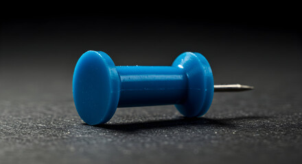 A single blue plastic pushpin lies on a dark surface, ready to secure your important notes and documents with style and efficiency.
