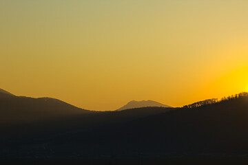 A stunning golden sunset casting long shadows over silhouetted hills and distant mountains.