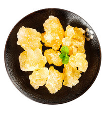 Handmade large grain yellow rock candy displayed on a black plate with mint leaves on a white...