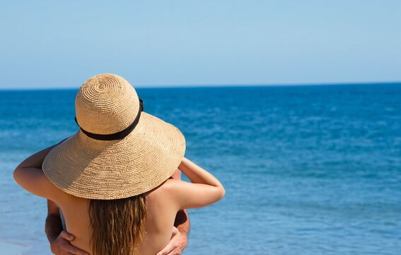 Woman hugging man on beach with straw hat and ocean view, copy space - Powered by Adobe