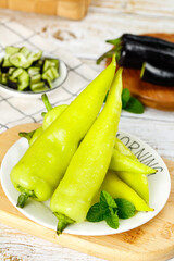 Fresh yellow tip chili peppers arranged on a plate with green herbs and vegetables in a cozy kitchen setting