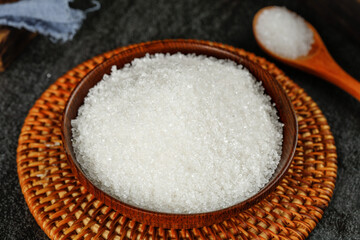 Granulated sugar displayed in a rustic bowl on a woven mat with a wooden spoon beside it