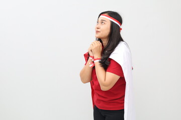 Indonesian women stand celebrating Indonesian independence while smiling and looking up while praying and posing with the red and white flag on their backs.