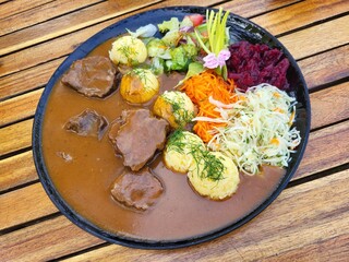 Traditionelles polnisches Gericht mit Rindfleisch, Kartoffeln, Bratensoße und buntem Gemüsesalat auf einem Holztisch serviert