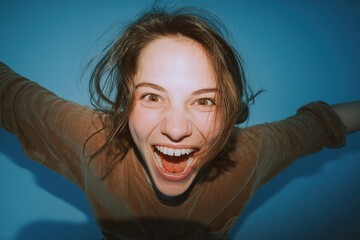 Joyful young woman expressing excitement with a wide smile against a blue background during a spirited moment indoors