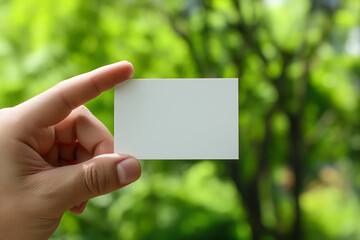 Hand holding blank white card against blurred green foliage background image