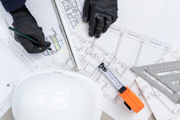 Top view of a contractor hands with pencil working on Architecture plans on desk of a construction site